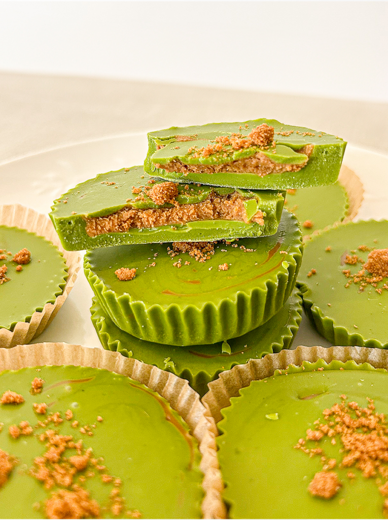 Green matcha cups with a brown Biscoff centre, some cut in half and stacked, others whole in paper liners. Crushed crumbs top the cups.