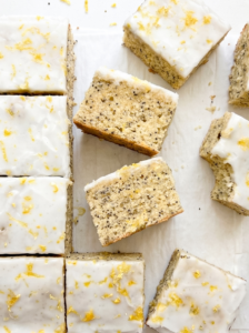 Square lemon poppyseed blondies with white lemon glaze and bright yellow lemon zest are arranged on white parchment paper.