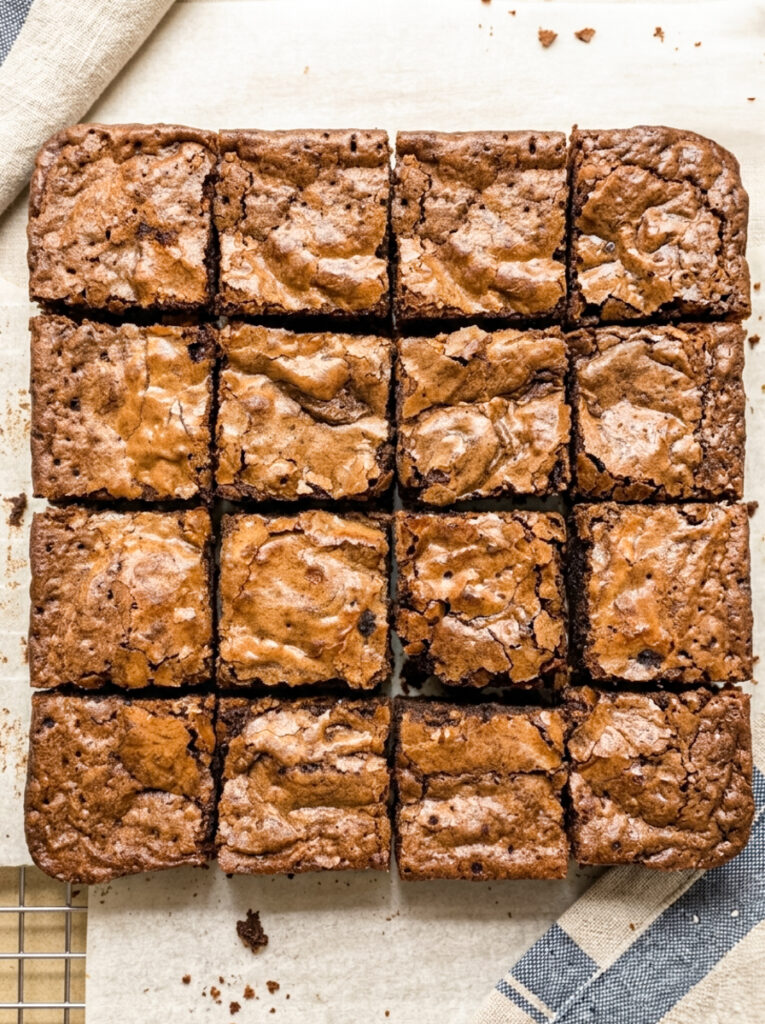 Sixteen square pumpkin swirl brownies with crinkly tops arranged in a grid on parchment paper.