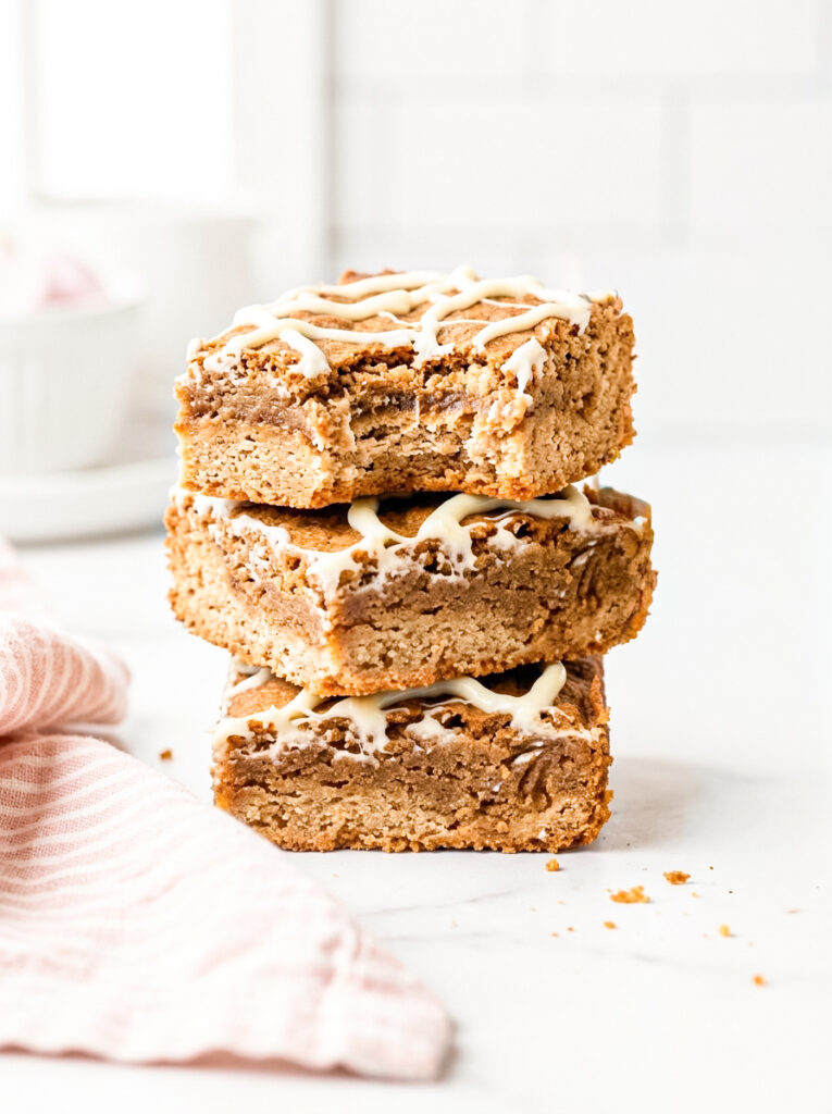 Dirty chai blondies with white glaze drizzle, stacked three high with a bite taken out.