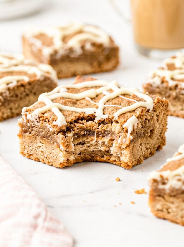 Dirty chai blondies topped with white glaze drizzle, showing a bite taken from one square.