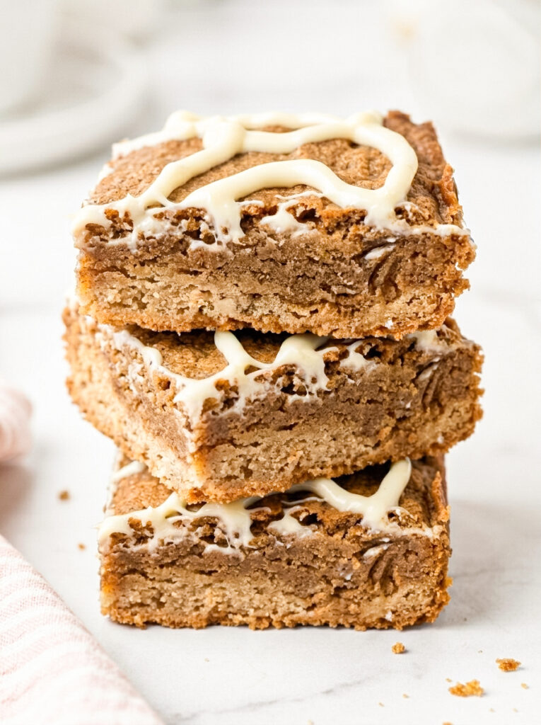 Dirty chai blondies stacked in three squares with a white glaze drizzle.