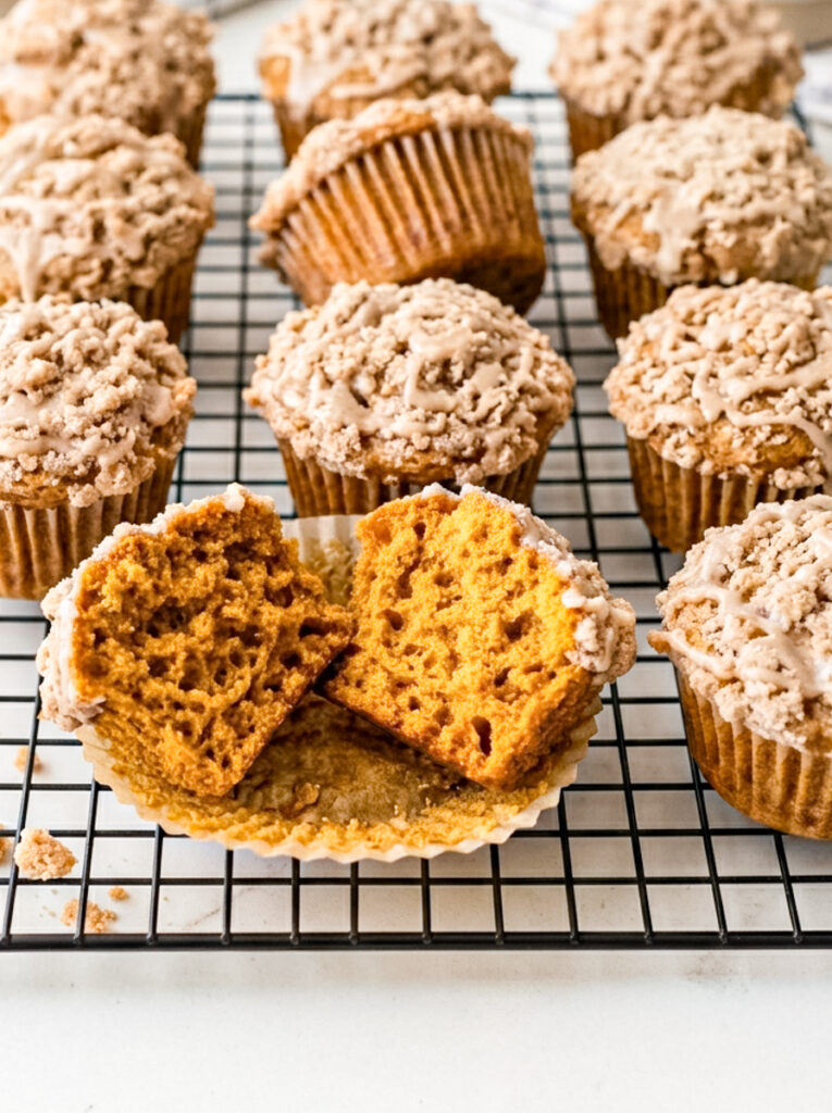 Pumpkin streusel muffins with crumble and glaze sit on a wire rack, with one muffin split open in the foreground.